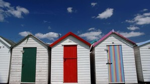 Une rangée de cabanes de plage aux portes de couleurs vives, se détachant sur un ciel bleu clair.