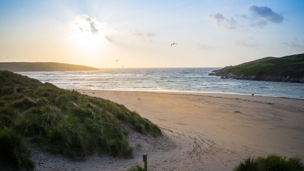 Une plage avec un ciel dégagé, des vagues et des dunes herbeuses.