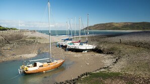Une rangée de bateaux amarrés sur une plage rocheuse, d’où l’on a une vue dégagée sur la mer et les collines lointaines.