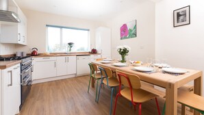 Une cuisine moderne avec des armoires blanches, un plan de travail en bois et un coin repas agrémenté de chaises colorées et d’une table en bois, le tout disposé pour accueillir quatre personnes.