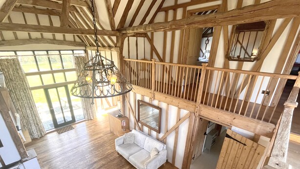A spacious loft with high ceilings, exposed wooden beams, a large chandelier, and a cozy seating area with a white sofa. - The Dairy Hall at Partridge Lodge (Woodbridge)