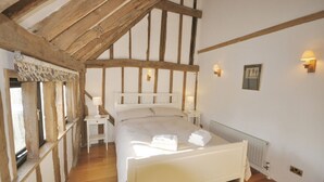 A bedroom with a wooden ceiling, a bed with white linens, bedside lamps, and a radiator. - The Dairy Hall at Partridge Lodge (Woodbridge)