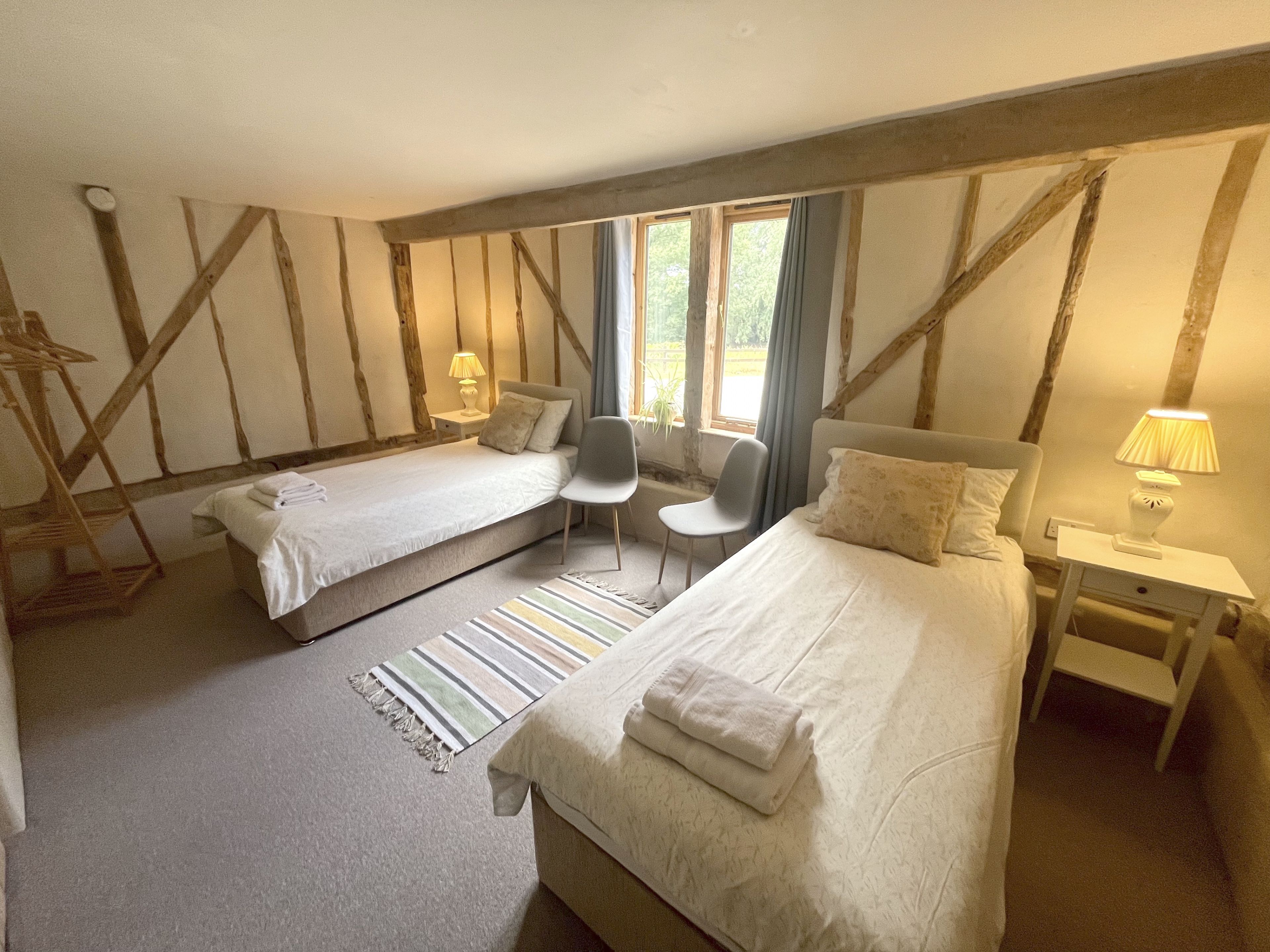 A bedroom with two beds, a chair, a nightstand, and a window.