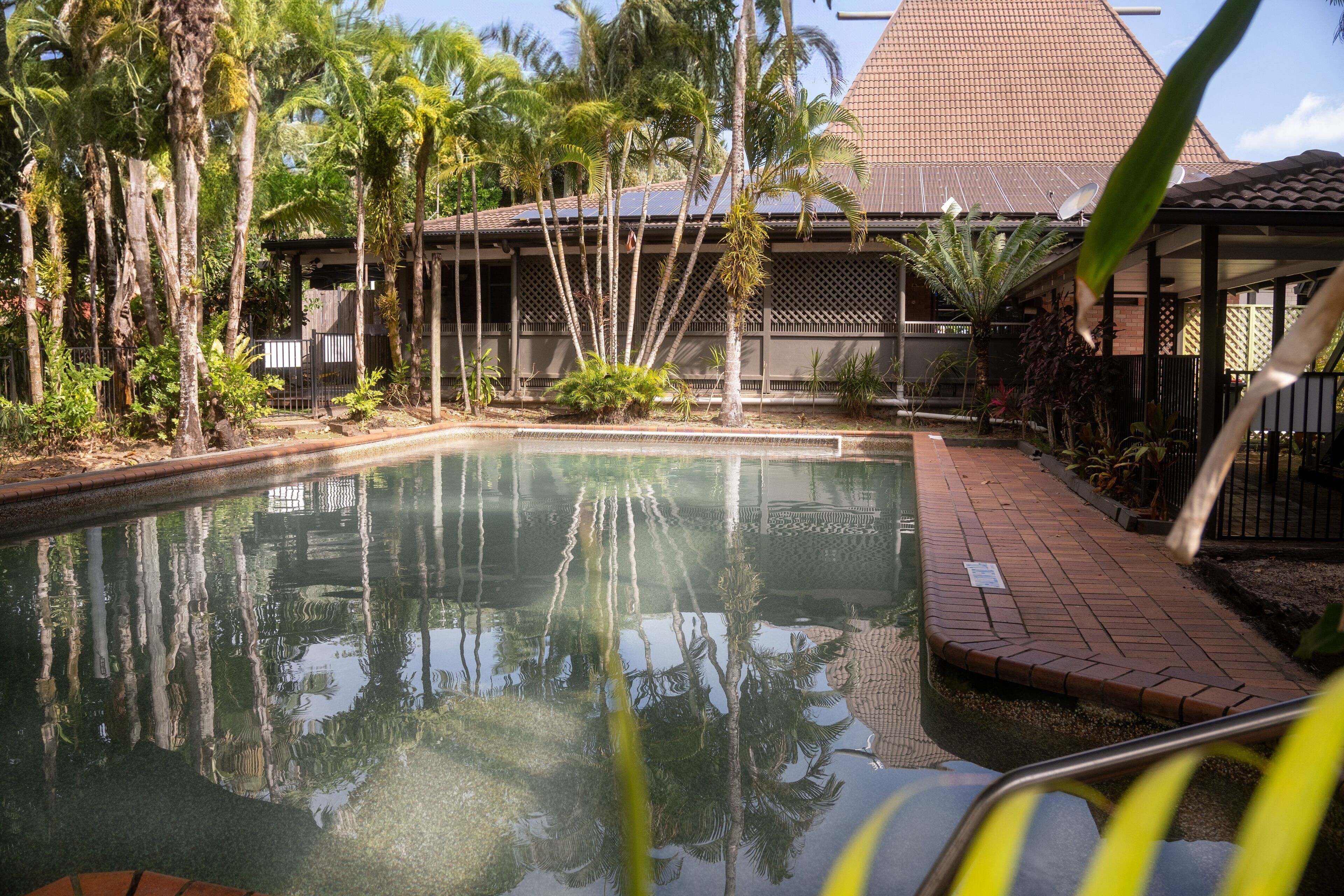 A pool surrounded by palm trees and a building with a tiled roof.