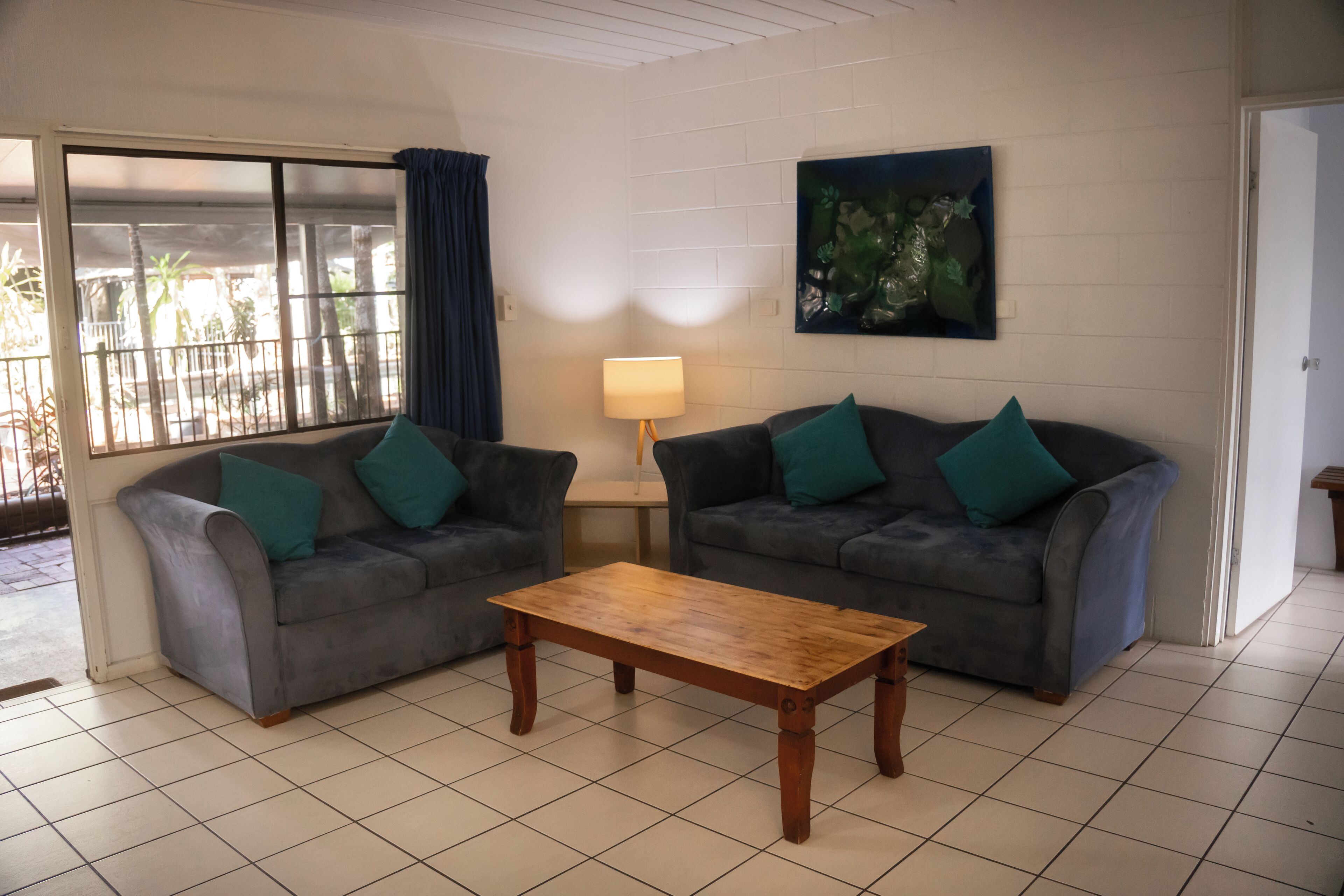 A living room with two grey sofas, a wooden coffee table, a lamp, and a large window with curtains.