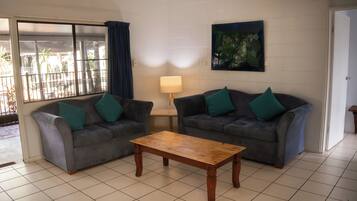 A living room with two grey sofas, a wooden coffee table, a lamp, and a large window with curtains.
