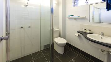 A bathroom with a glass shower enclosure, a toilet, and a sink with a mirror above it.