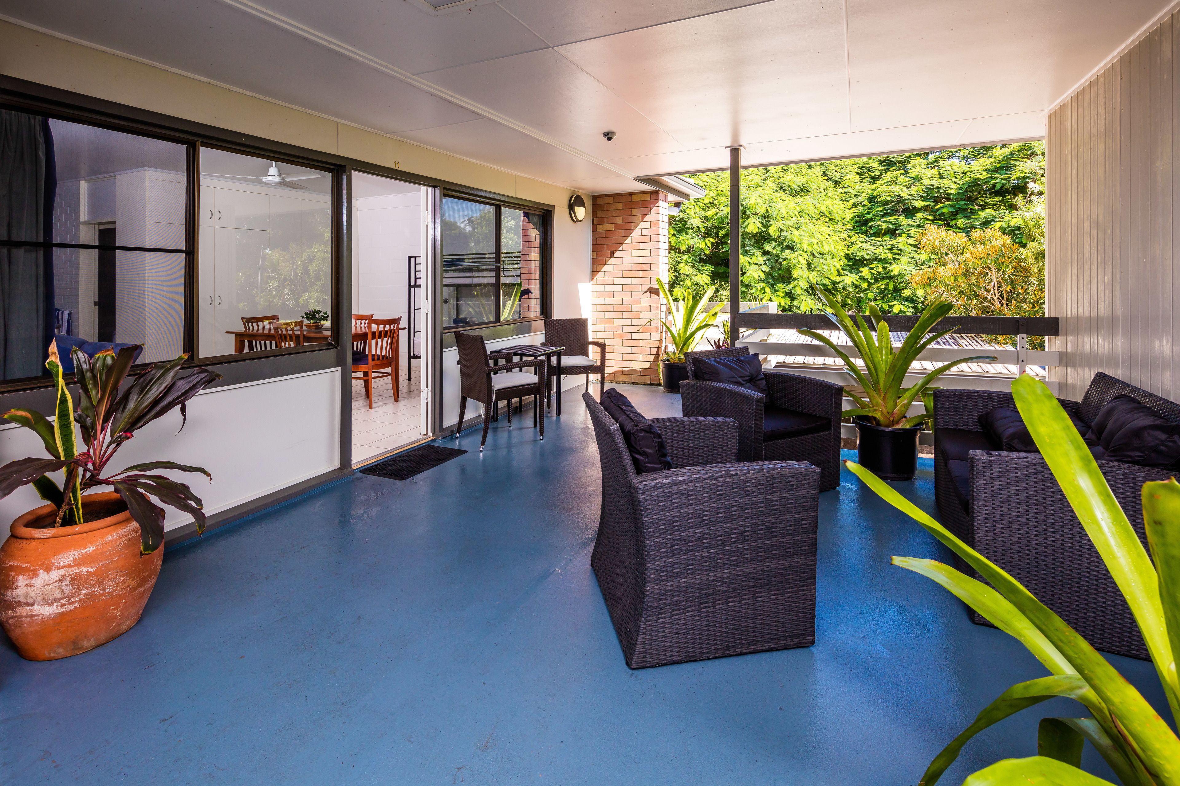 A covered outdoor area with wicker furniture, a table, chairs, and potted plants.