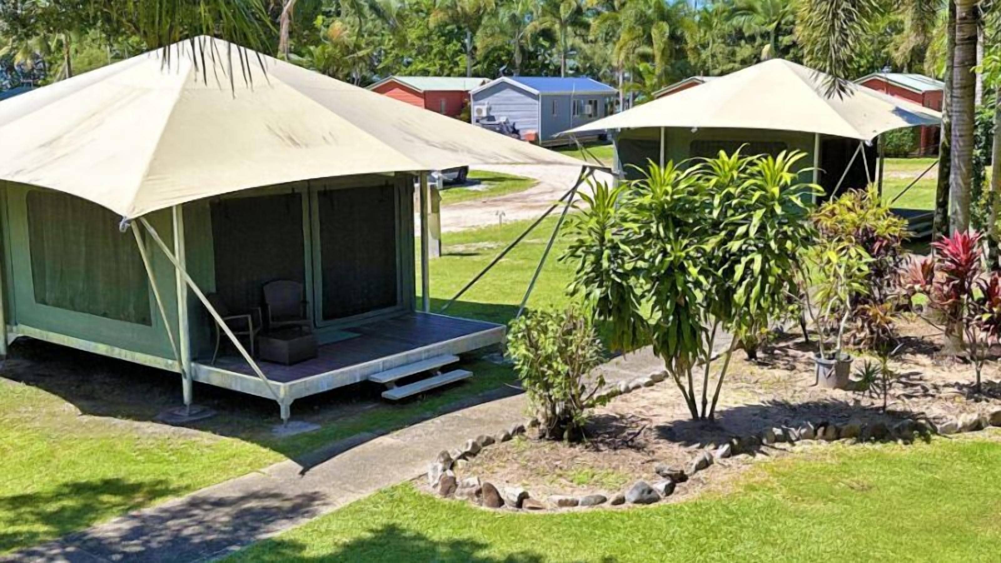 A camping site with two tents, each with a porch and seating area, surrounded by greenery and a small garden.