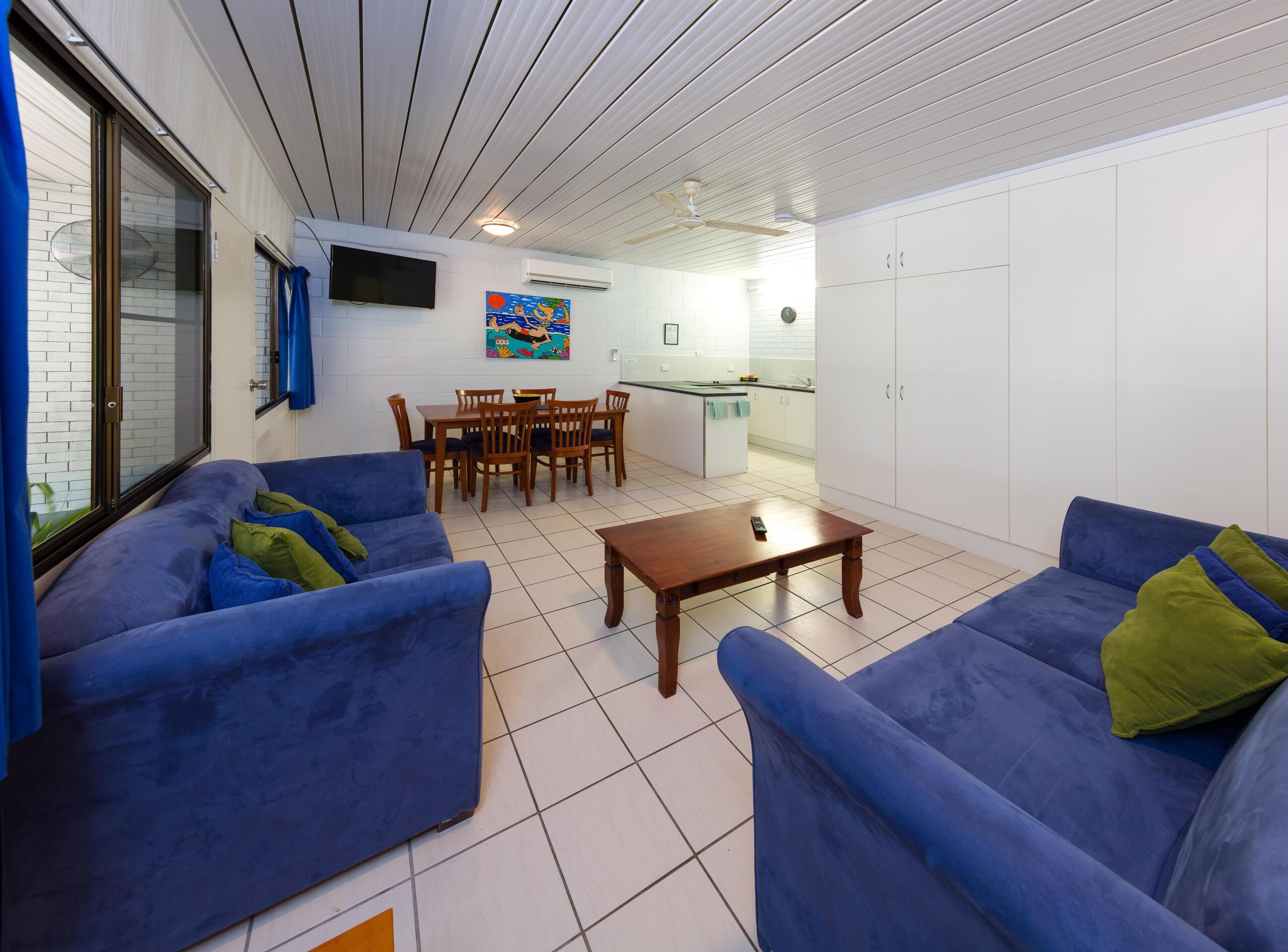 Una sala de estar con sofás azules, una mesa de centro de madera y un comedor con sillas y mesa de madera.