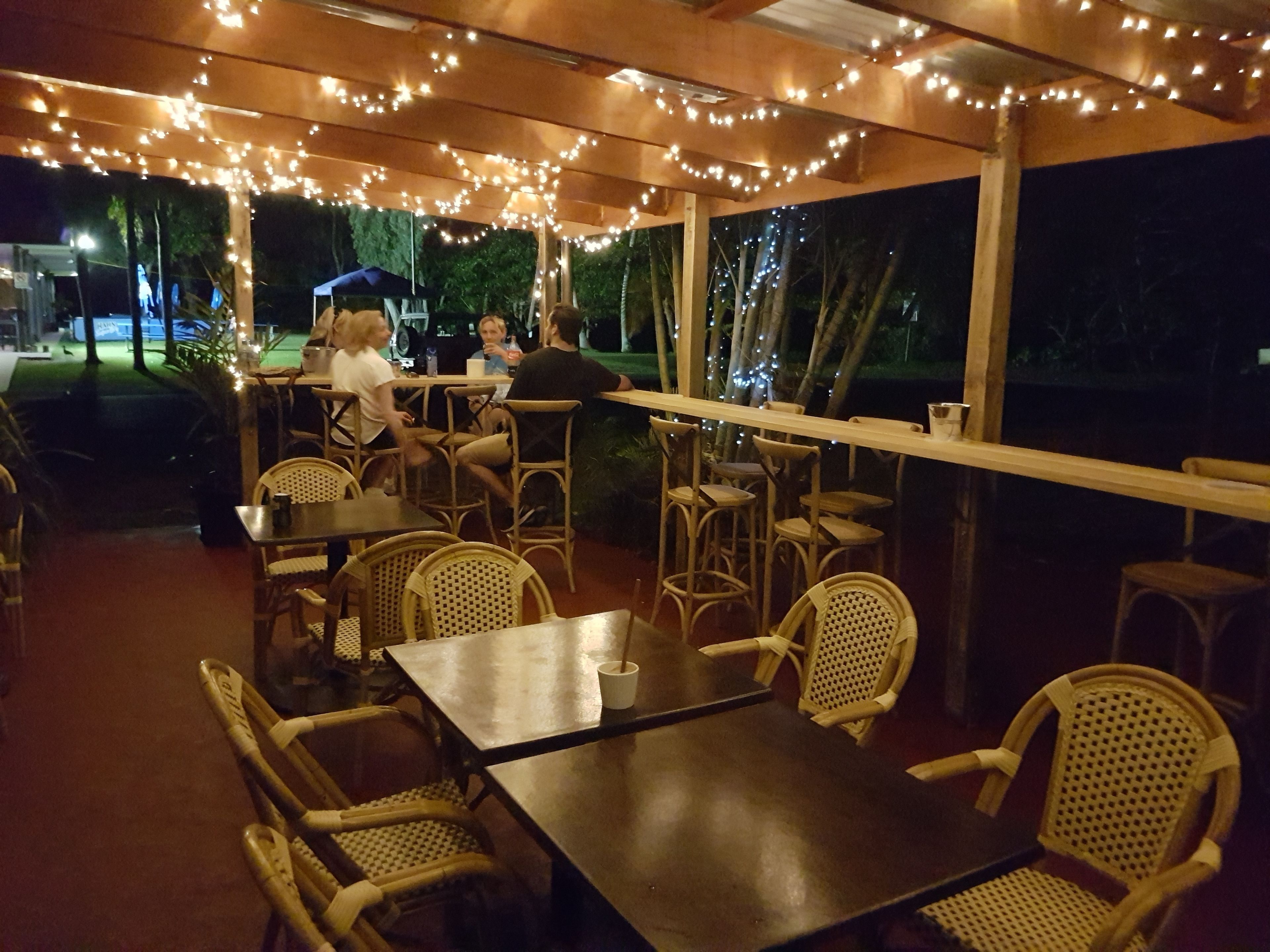 An outdoor dining area with tables and chairs, string lights overhead, and a view of the night sky.