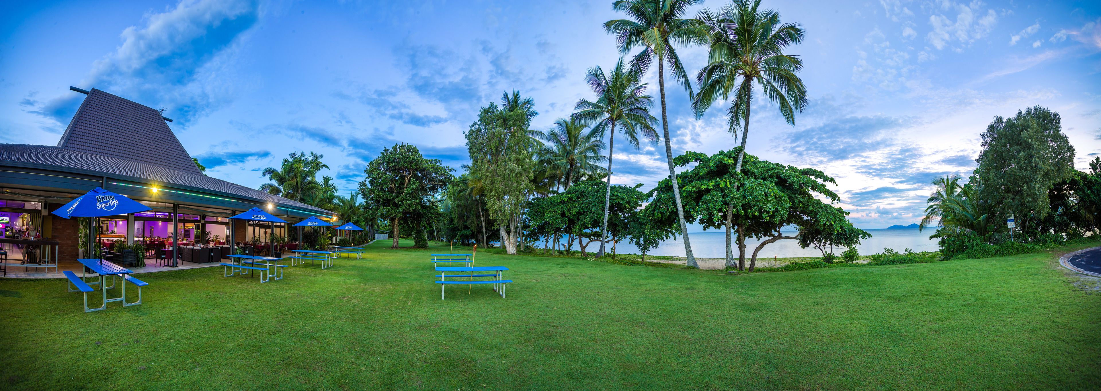 Un restaurante con terraza, palmeras y vistas al agua.
