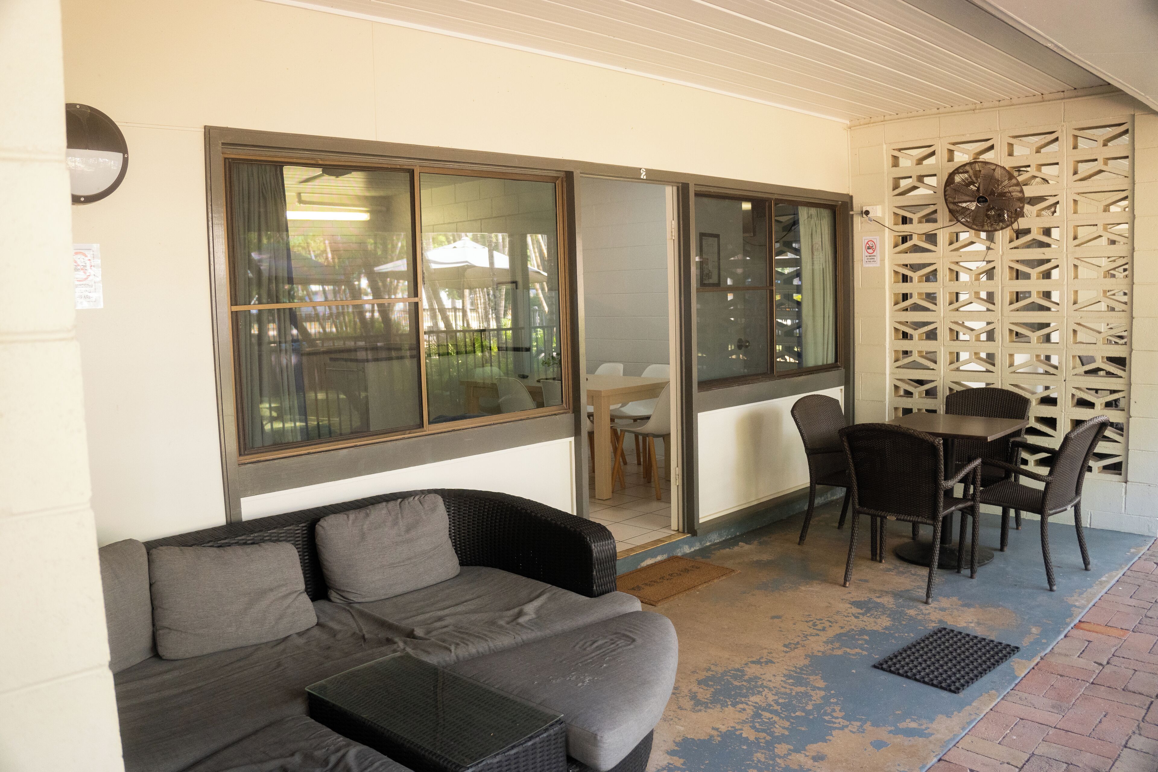 A covered outdoor seating area with a sofa and chairs, a table, and a decorative wall.