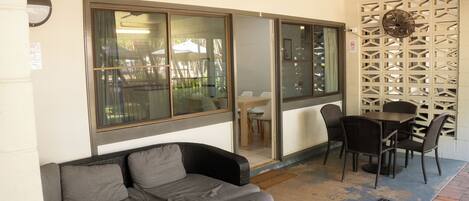 A covered outdoor seating area with a sofa and chairs, a table, and a decorative wall.