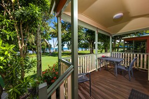 A covered outdoor area with a wooden deck, metal chairs, and a table. - King Reef Resort (Kurrimine Beach)