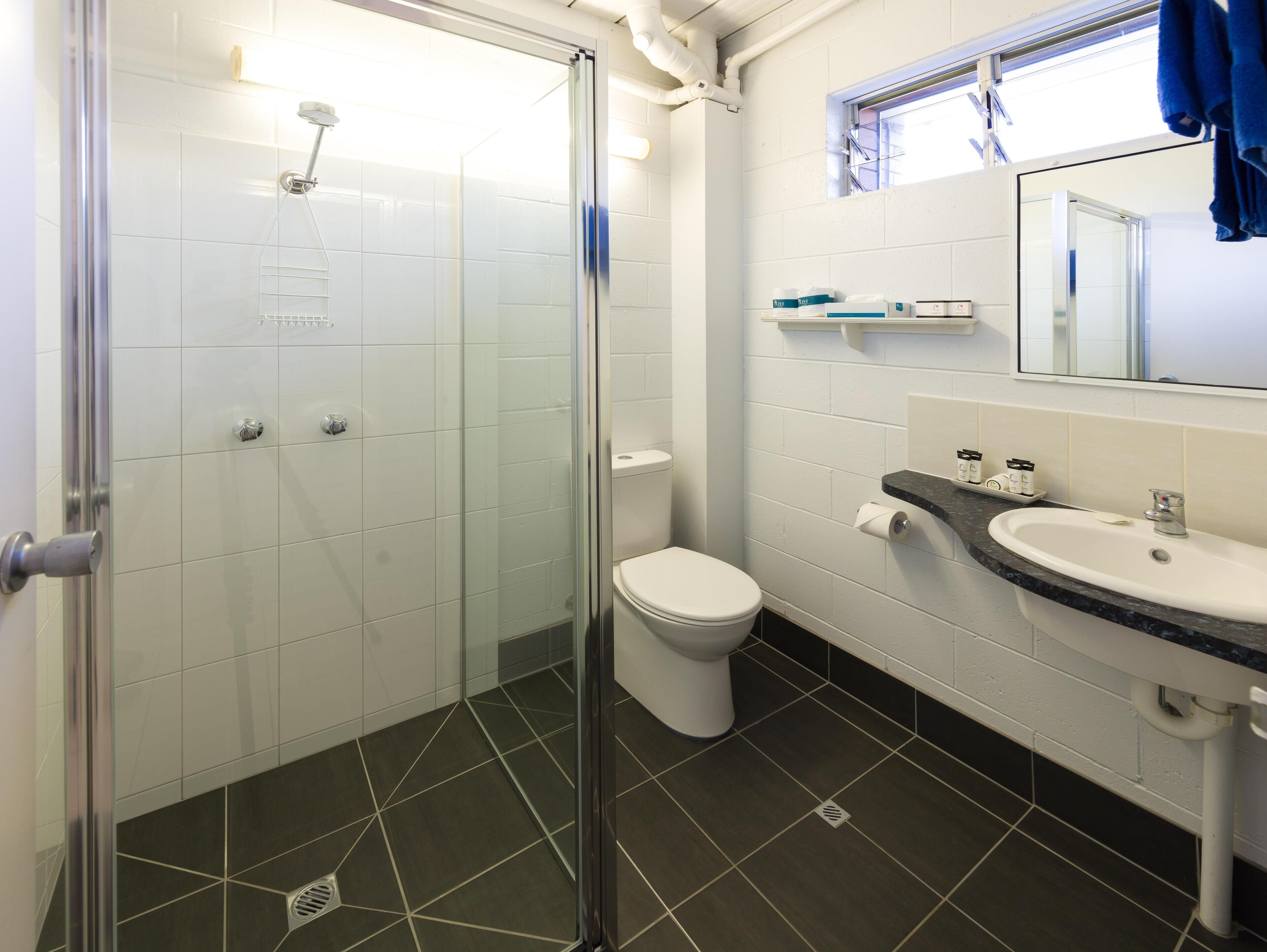 A bathroom with a glass-enclosed shower, a toilet, a sink, and a mirror.