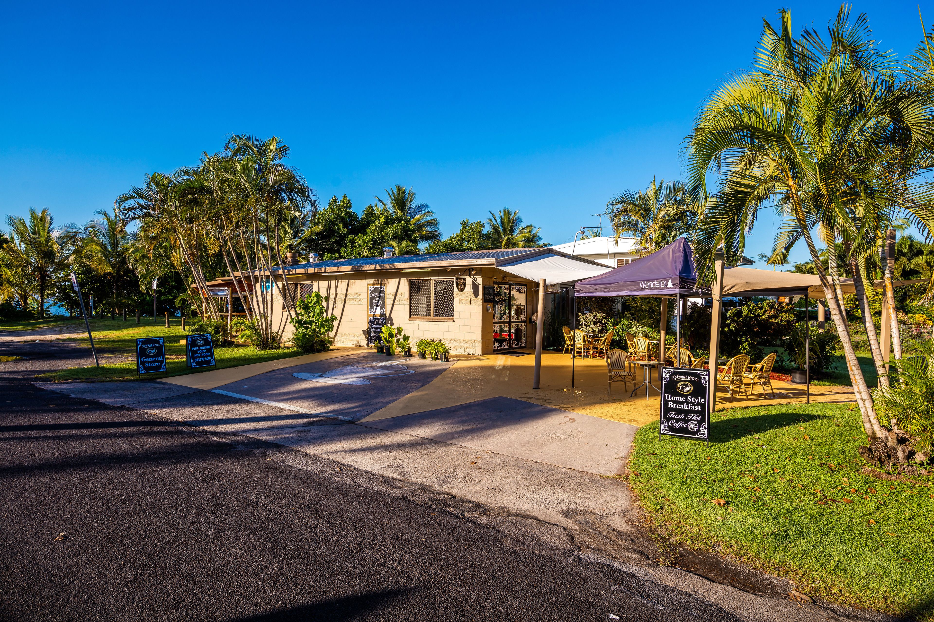 A building with a covered outdoor seating area, palm trees, and a sign advertising a home-style breakfast.