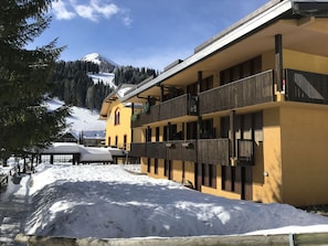 A yellow building with balconies, a snow-covered ground, and a mountain in the background.
