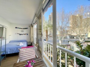 A balcony with a bed, a small table, and a view of a cityscape with buildings and trees. - BLUE APARTMENT R022 (Benidorm)