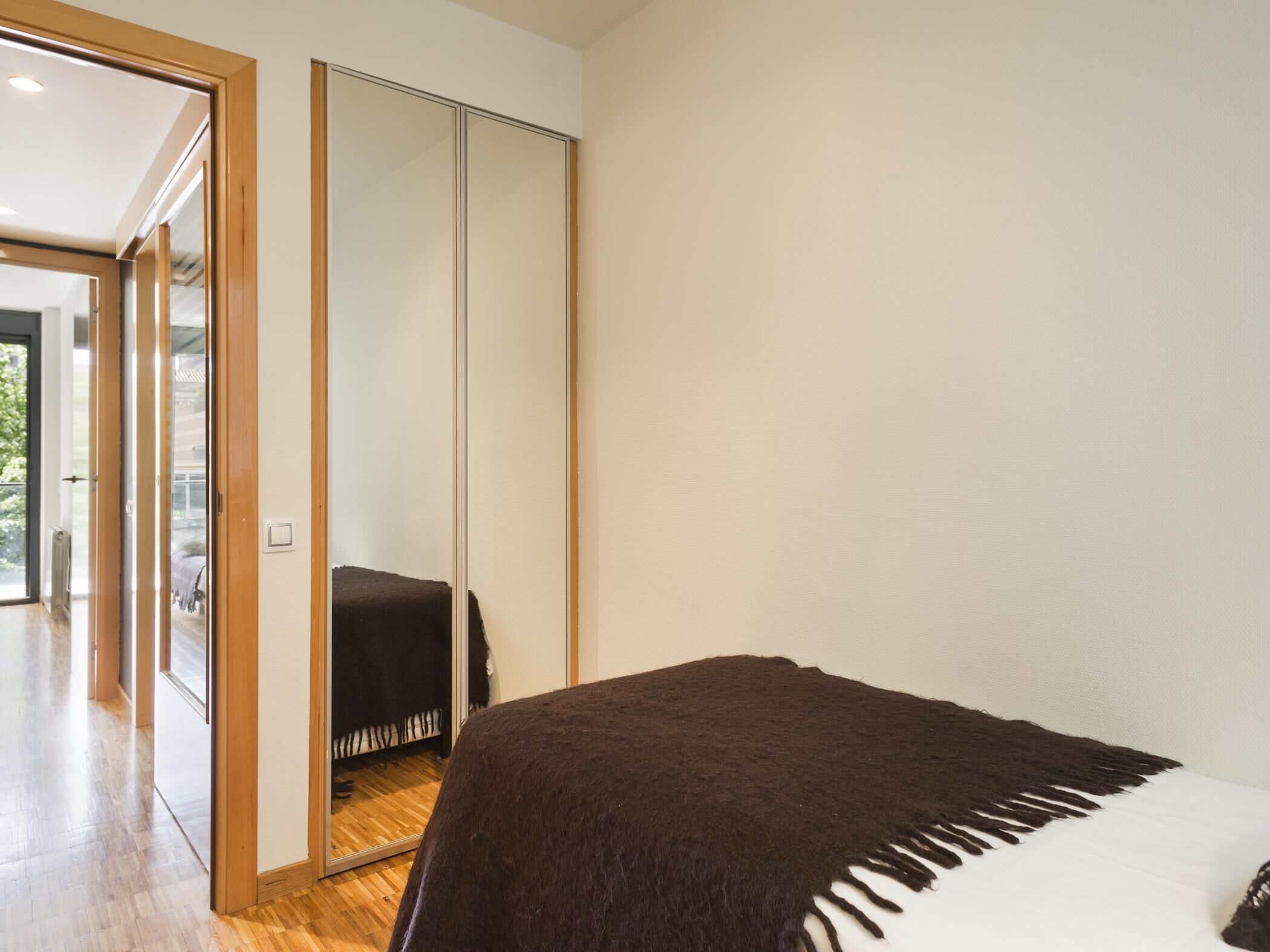 Un dormitorio con un espejo grande, suelo de madera y una cama con un edredón oscuro.