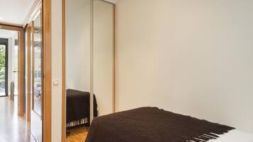 Un dormitorio con un espejo grande, suelo de madera y una cama con un edredón oscuro.