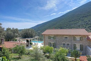 A stone building with a tiled roof, a pool, and a mountainous backdrop.