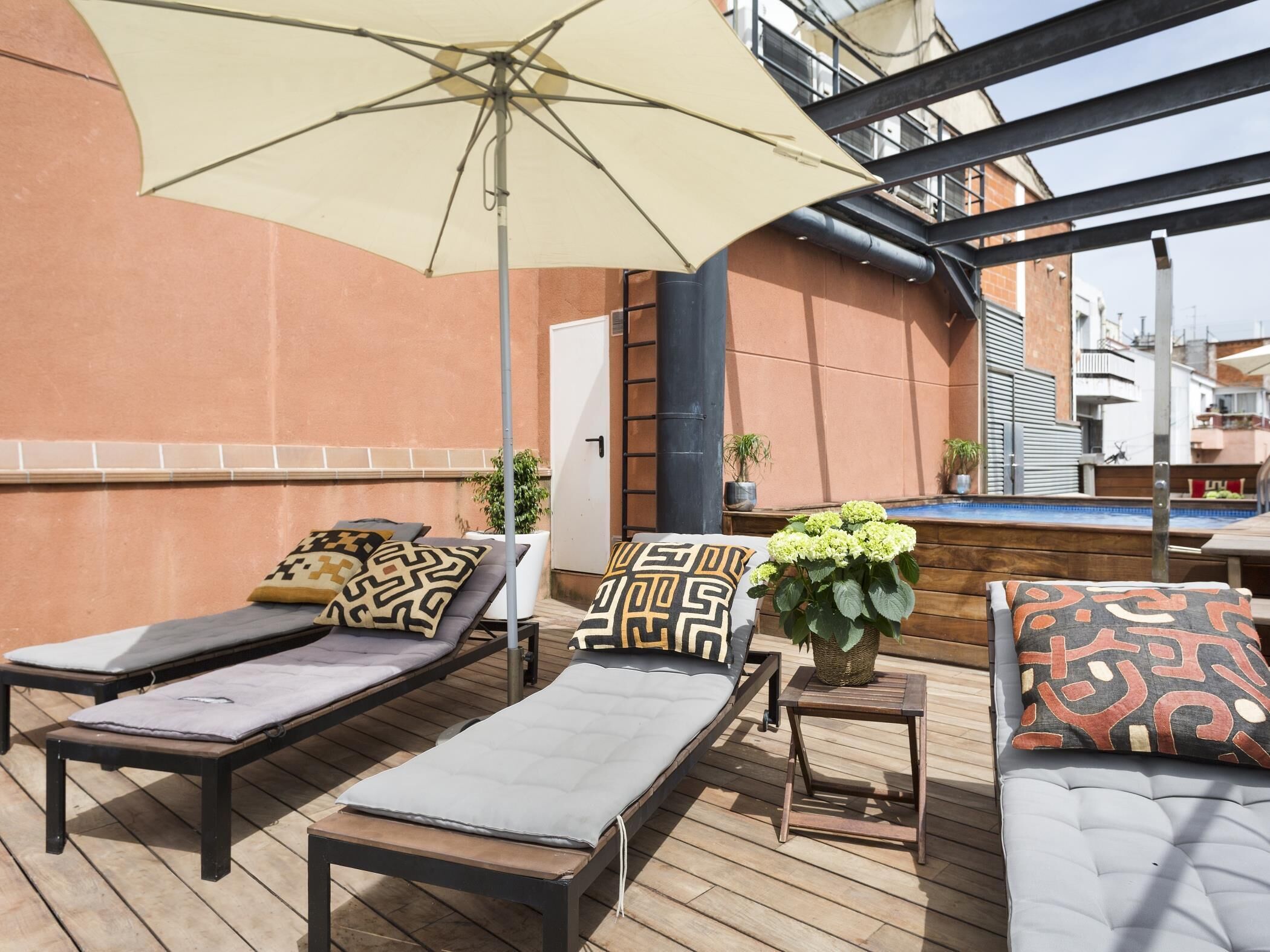 Un área de lounge al aire libre con tumbonas, un parasol grande y una pequeña mesa con un jarrón de flores.