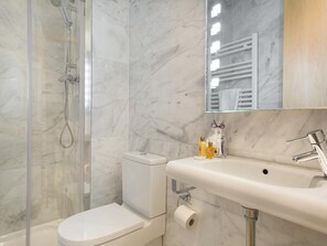 A bathroom with a glass-enclosed shower, a white toilet, a sink with a mirror above it, and toiletries on the sink.