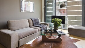 A modern living room with a sofa, a glass coffee table, and a large window with a view of a balcony.