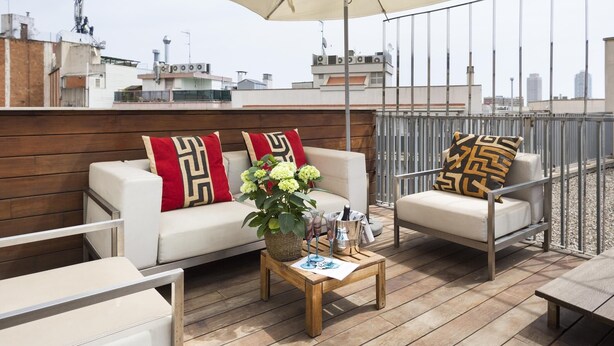 A rooftop terrace with a wooden deck, white sofas, and a large umbrella.