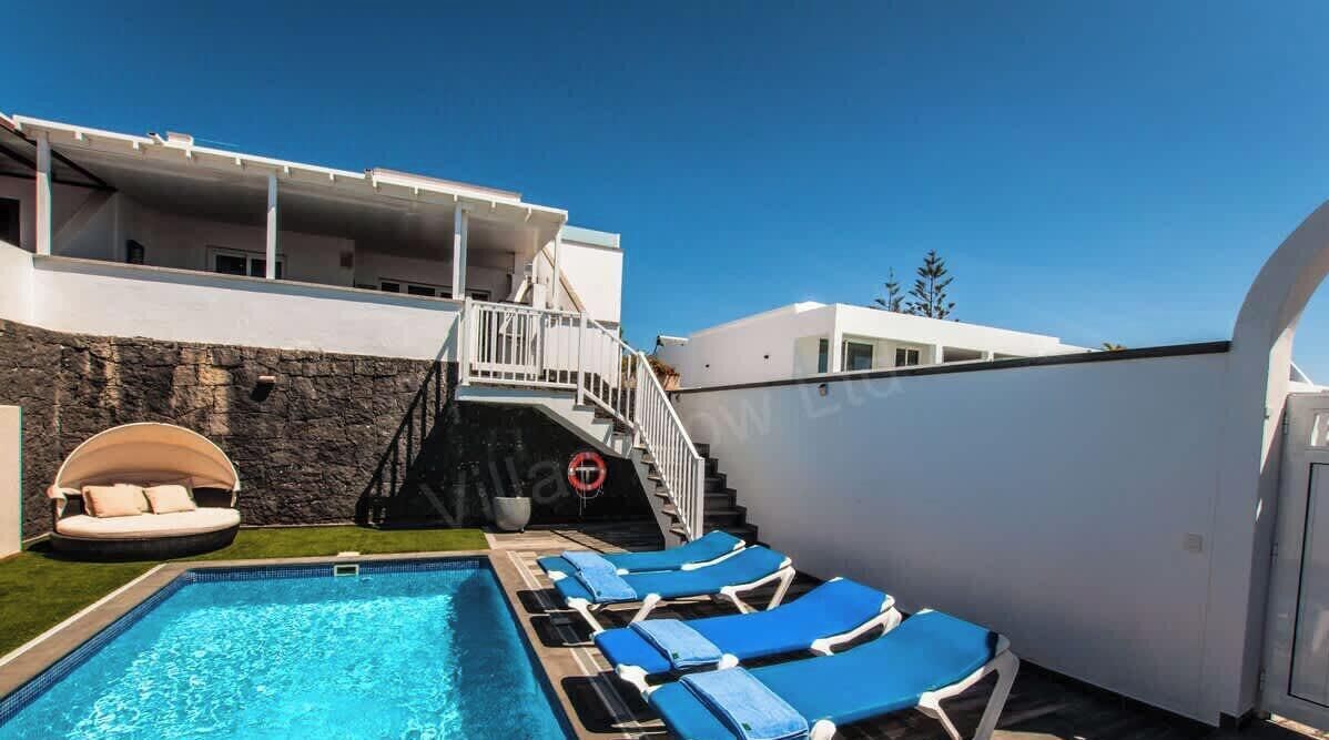 Une piscine avec des chaises longues, un mur en pierre et un escalier menant à un niveau supérieur.