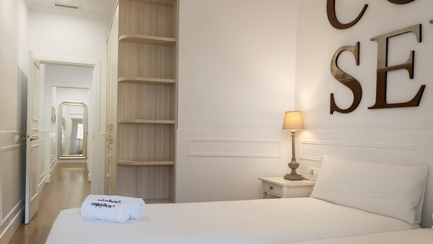 Una habitación de hotel con una cama grande, una mesita de noche con lámpara, un armario y un espejo.
