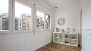 Una habitación amplia con ventanas grandes, un reloj de pared blanco y una estantería blanca con objetos decorativos.