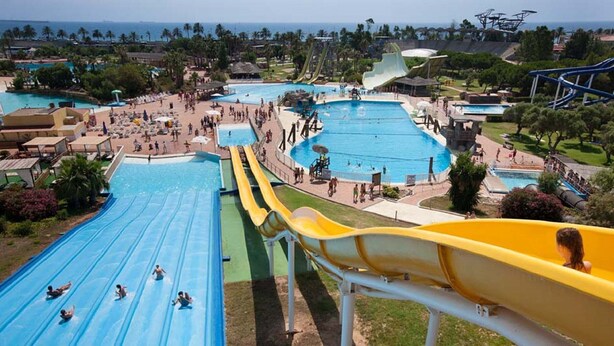 Un parc aquatique doté de nombreux toboggans et de plusieurs piscines, entouré de verdure et surplombé d’un ciel dégagé.