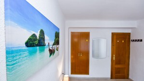 Une chambre d’hôtel avec une grande fresque murale aux motifs tropicaux, des portes en bois et une petite table avec une lampe.