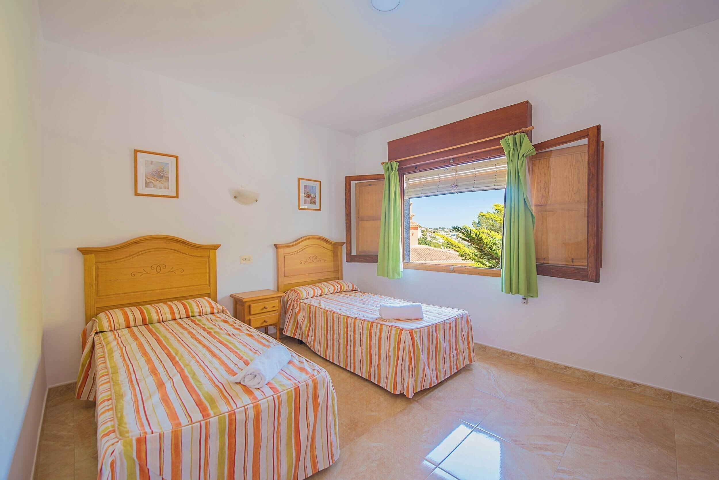 A room with two beds, a window with curtains, and a small table.