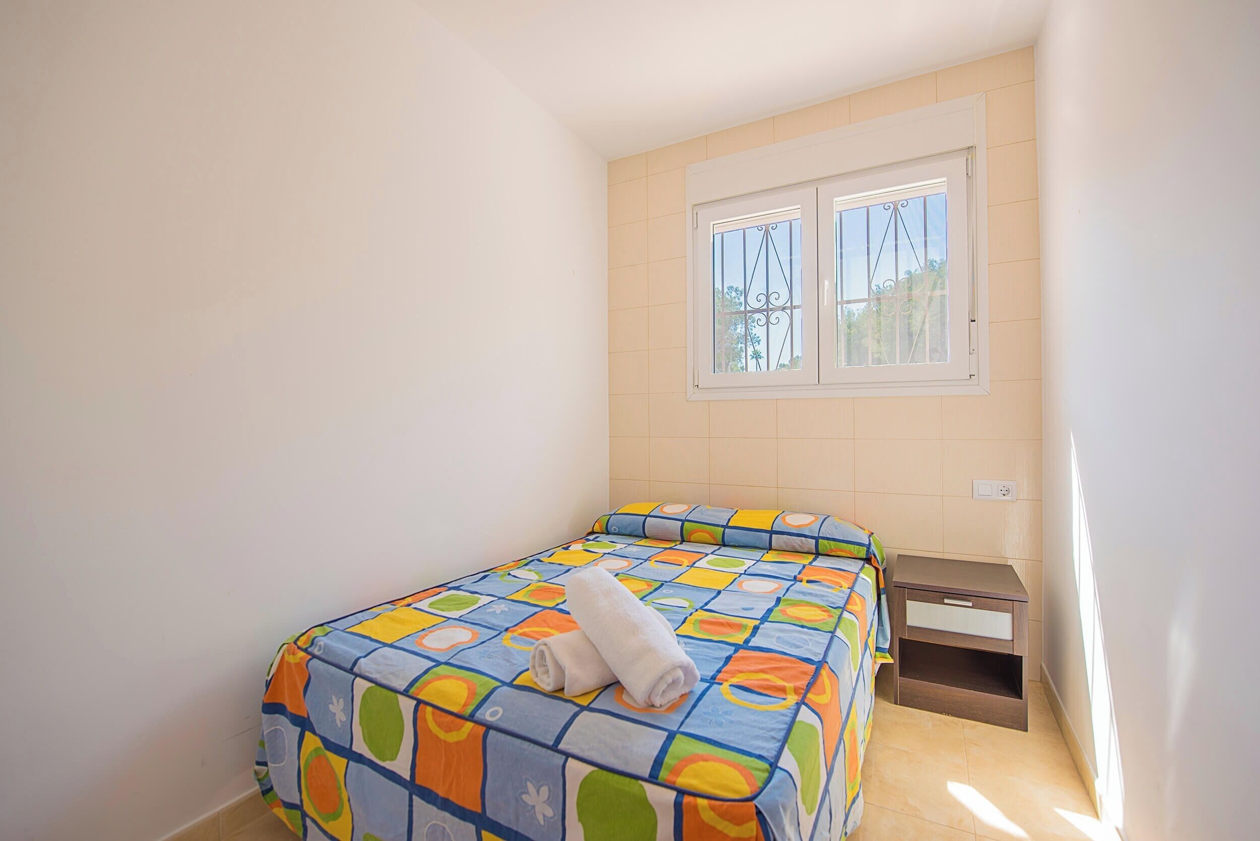 A small, clean room with a bed, a nightstand, and a window.
