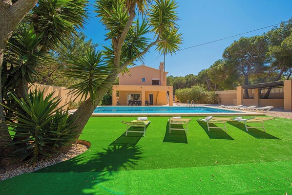 A modern house with a swimming pool, surrounded by artificial green grass and palm trees.