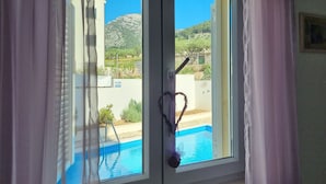 Une fenêtre donnant sur une piscine et un paysage montagneux.