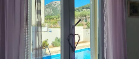 A window with a view of a swimming pool and a mountainous landscape.