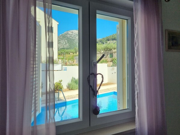 A window with a view of a swimming pool and a mountainous landscape.