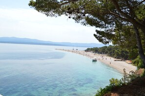 A coastal beach with clear water, a sandy shore, and a line of trees.