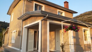 Ein zweistöckiges Haus mit Balkon, Schornstein und einem hängenden Blumentopf.