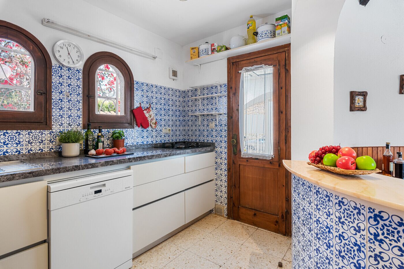 A kitchen with a wooden door, white cabinets, and blue patterned tiles.