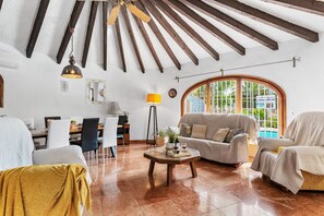 A spacious living area with a high ceiling, a dining table, and a sofa set.