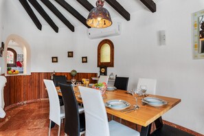A dining area with a wooden table, white chairs, and a hanging light fixture. - Villa Axel - PlusHolidays (Calpe)