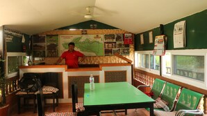 Restaurante com esquema de cores verde e branco, apresentando um mapa na parede, um balcão com uma pessoa atrás e disposição de mesas.