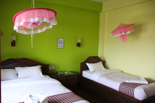 A hotel room with two beds, a nightstand, a telephone, and a wall-mounted light fixture. - Sweet Home (Sauraha)