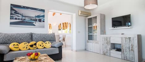 Een moderne woonkamer met een bank, een salontafel met fruit, een televisie en een schilderij van een gebouw.