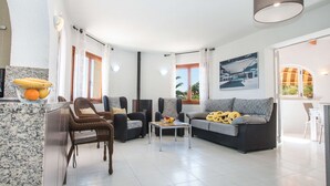 Ein geräumiger Wohnbereich mit einer Couch, Sesseln, einem Couchtisch und einem Essbereich mit Tisch und Stühlen.